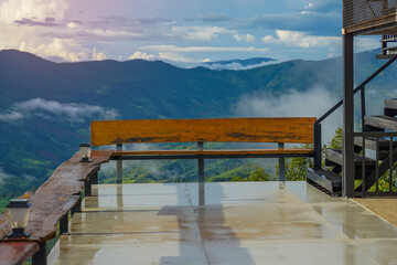 A long wooden bench serves as a balcony to sit and relax, admiring the mountain view and the rainy season mist, white streaks covering the mountain like fluffy clouds.   
