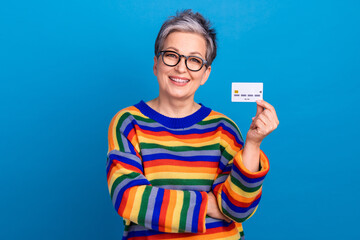 Photo of friendly positive grandmother toothy smile arm hold debit card isolated on blue color...