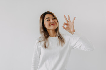 Asian Thai woman smiling and showing okay sign gesture, giving positive feedback, isolated on white background in winter.