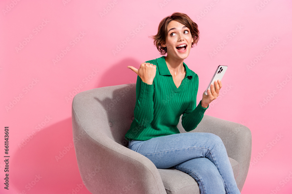 Wall mural Photo of girl pointing finger empty space looking interested using smartphone app for cleaning service isolated on pink color background