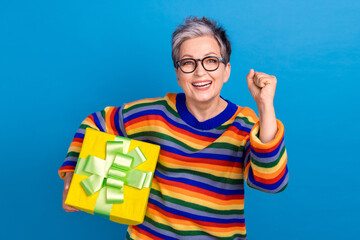 Naklejka premium Portrait of delighted positive person hold desirable giftbox raise fist isolated on blue color background