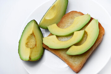 Fried toast with slices of green avocado. A delicious lunch of bread and ripe avocado.