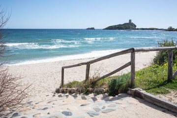 rocky descent to the beach, clear water and fortification in the background