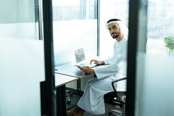 Fototapeta premium handsome man with dish dasha working in his business office of Dubai. Portraits of a successful businessman in traditional emirates white dress. Concept about middle eastern cultures.