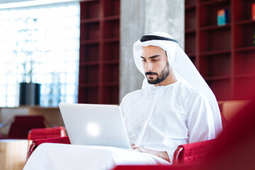 handsome man with dish dasha working in his business office of Dubai. Portraits of a successful businessman in traditional emirates white dress. Concept about middle eastern cultures.