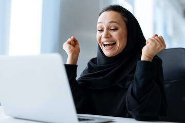 beautiful woman with abaya dress working on her computer. Middle aged female employee at work in a business office in Dubai. Concept about middle eastern cultures and lifestyle