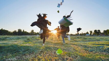 Cheerful graduates students run throwing notebooks after school at sunset.