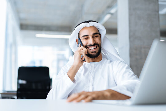 handsome man with dish dasha working in his business office of Dubai. Portraits of a successful businessman in traditional emirates white dress. Concept about middle eastern cultures.