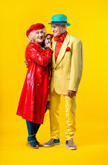 Fototapeta premium Beautiful senior old couple wearing fancy party clothes acting in studio on a colored background. Conceptual image about third age and seniority, old people feeling young inside.