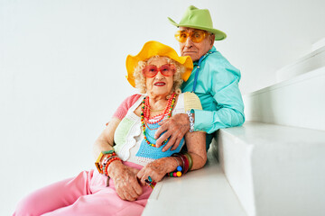 Beautiful senior old couple wearing fancy party clothes acting in studio on a colored background....