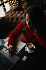 woman in a red sweater sits in a cafe in winter and works on the Internet