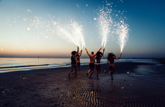 Group of friends having fun running on the beach with sparklers