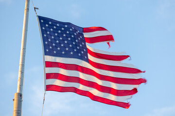 ripped American flag on flagpole blowing in wind