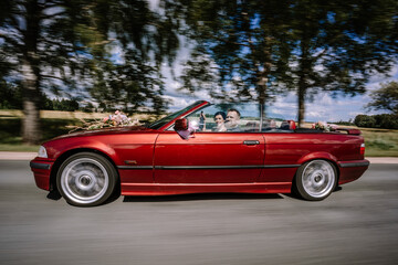 A newlywed couple drives in a bright red convertible