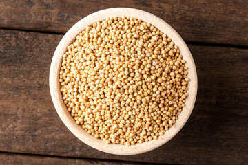 White mustard seeds in bowl on wooden table. Close up. Top view