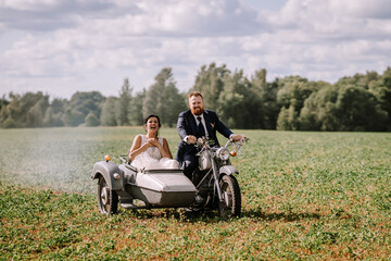 The bride and groom ride a motorcycle with a sidecar through the countryside