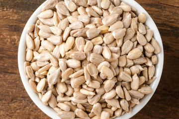 Peeled sunflower seeds in bowl on rustic wooden table. Top view