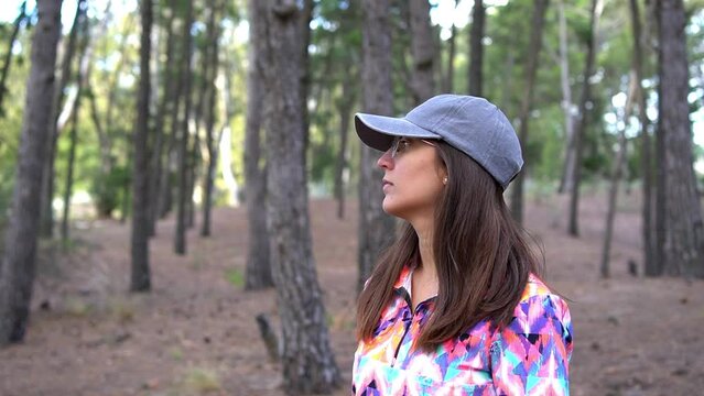 Young adult Latina woman in sportswear cap and glasses looking attentively at a forest of environmentally damaging exotic pines in Argentina. Slow motion shot with space for text.