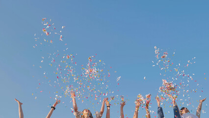 Tossing colorful paper confetti from the hands of young people.