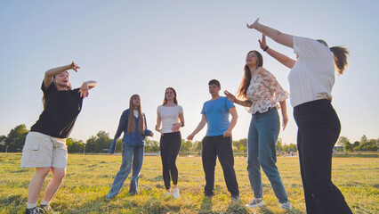 Funny jolly friends dancing in the city meadow in the evening.