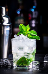 London Mint Swizzle cocktail drink with gin, juice, syrup, soda, fresh mint and crushed ice. Black bar counter background with bottles