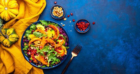 Healthy autumn pumpkin salad with lettuce, arugula, pomegranate seeds and walnuts. Comfort slow food. Blue background. Top view - obrazy, fototapety, plakaty