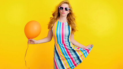 Excited fashionable woman dancing with balloon having fun for celebrate, entertainment. Carefree playful smiling redhead lady, trend makeup, colorful outfit for ad, fashion, party. Studio on yellow