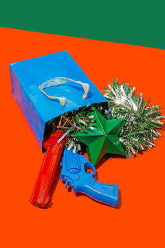 Blue carton bag placed on red surface with tinsel, colorful toy guns and green star against green background