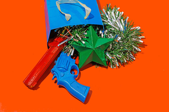 Blue carton bag placed on red surface with tinsel, colorful toy guns and green star