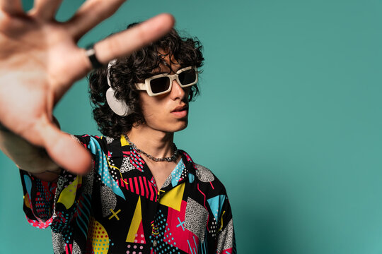 Trendy ethnic young man with headphones and sunglasses near turquoise backdrop