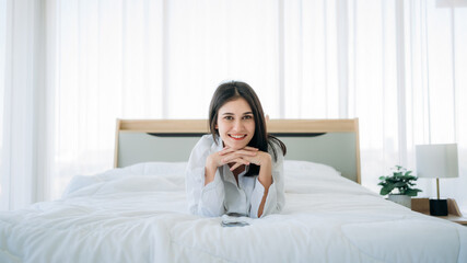 Young Woman Waking Up and play phone in Cozy Bedroom at Home. Beautiful Girl Smiling and Relaxing in Bed after Waking Up.