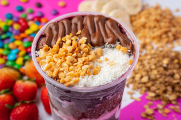 close up of acai or açaí cup with topping chocolate and nuts in colorful background