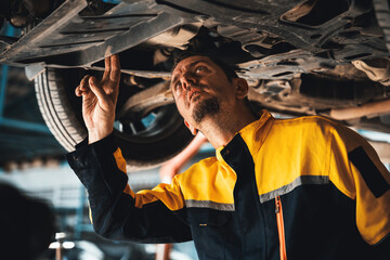Vehicle mechanic conduct car inspection from beneath lifted vehicle. Automotive service technician...