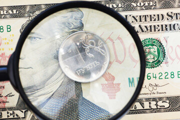 10 dollar bill and 1 Russian ruble coins under a magnifying glass.