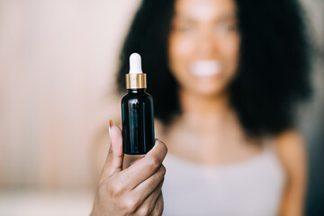 Mockup bottle of serum in hands of african woman. Beauty blogging, skin care concept