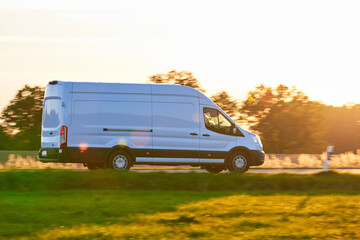 White Van driving fast on a country road. Delivery Van driving at sunset in autumn season.