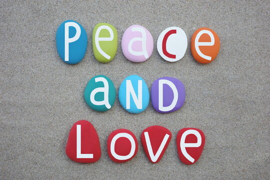 Peace and love, creative slogan composed with hand painted multi colored stone letters over beach sand