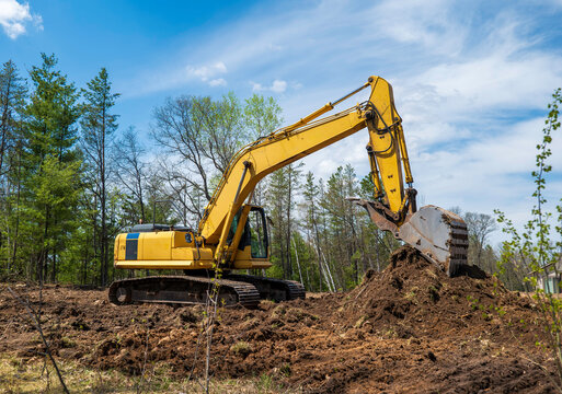 A yellow excavator at a future new home building site with its bucket resting on a pile of dirt.