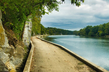 Autumn landscape of C&O Canal Towpath Trail in Maryland, curving between rocky cliffs and the Potomac River beneath a cloudy sky.