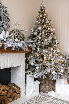 A Christmas tree decorated with white toys and balls near a decorated fireplace