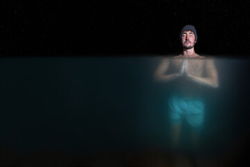 focused meditating man doing bath in cold water under the stars with under water view at night