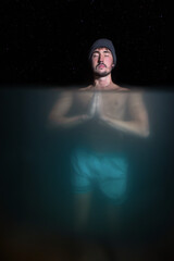 focused meditating man doing bath in cold water under the stars with under water view at night