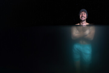 smiling man doing bath in cold water holding his body because of cold with under water view under the stars at night