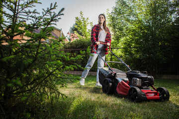 Female gardener working in autumn, cutting grass in backyard. Concept of gardening, work, nature. Housework, gardening and country life. Home garden grass cutting woman mowing with lawn mower.
