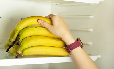 Female hand holding a bunch of bananas on a shelf in the refrigerator