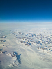 Areal view of snow and mountain peaks in Greenland on a sunny day with blue sky