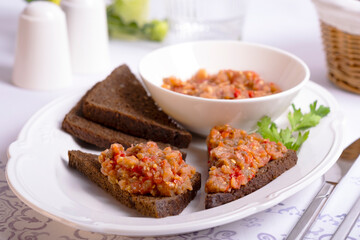 appetizer of eggplant and tomato on slices of dark bread on a white dish stands on a table with a white tablecloth