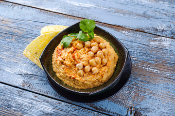 Traditional Indian chickpeas dip with pita bread and herbs as close-up in a design bowl with copy space