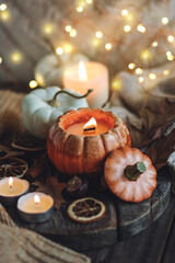 Autumn composition with burning candles, mini munchkin pumpkins, warm wool knitted sweater on the wooden windowsill. Dark colours. Cozy home atmosphere, Thanksgiving decor, fall inspiration. Close up