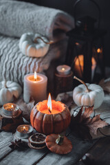 Autumn composition with burning candles, mini munchkin pumpkins, warm wool knitted sweater on the wooden windowsill. Dark colours. Cozy home atmosphere, Thanksgiving decor, fall inspiration. Banner